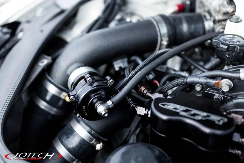 A close-up view of a Jotech Motorsports performance engine bay featuring a blow-off valve and custom boost piping.