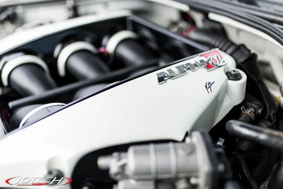 Close-up of a white Alpha Performance intake manifold in a high-performance engine bay, likely a Nissan GT-R.
