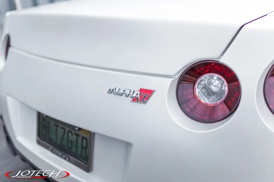 Close-up of the rear of a white Nissan GT-R with an Alpha X badge and a Jotech Motorsports license plate frame.