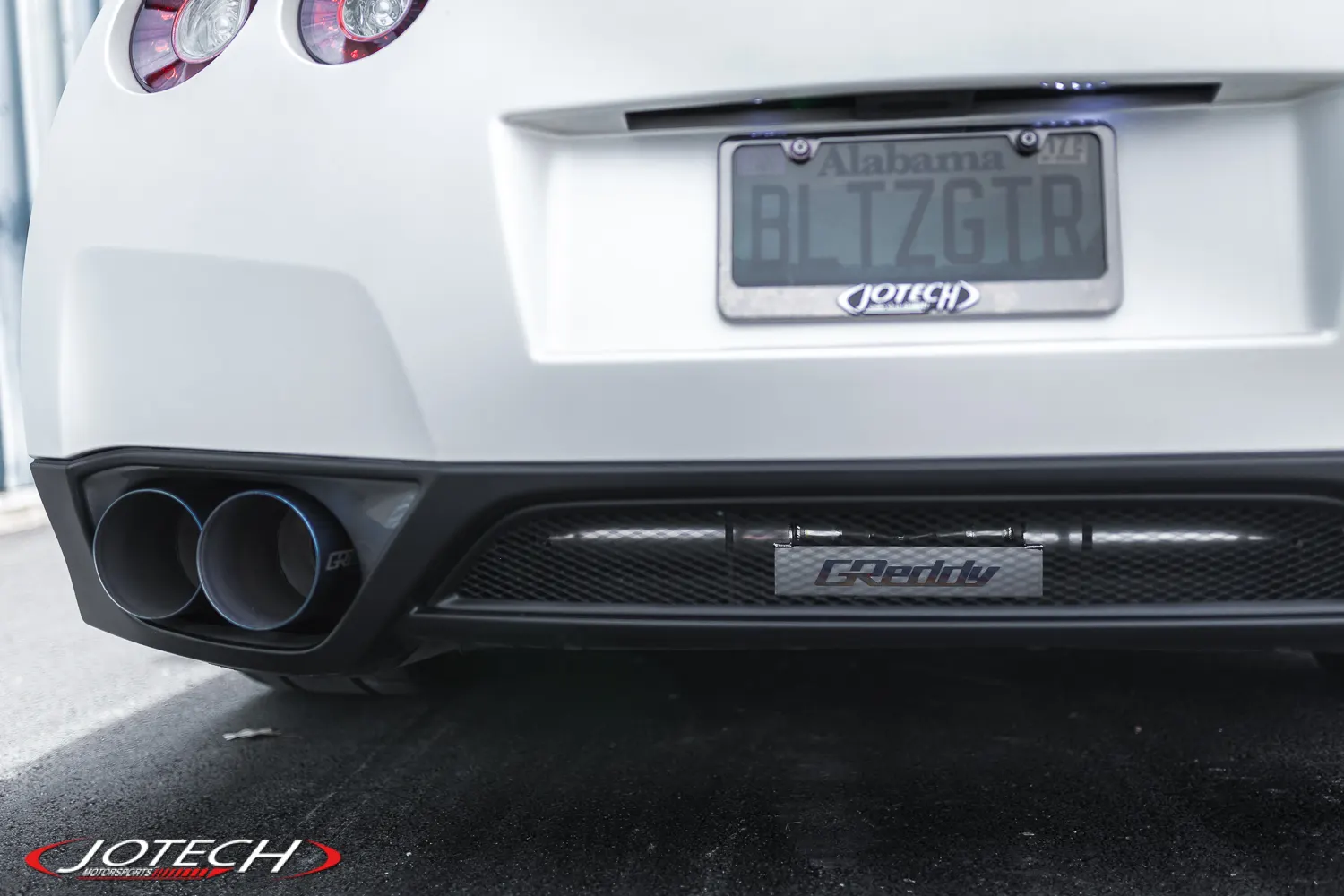 Rear view of a white Nissan GT-R showcasing GReddy exhaust system and dual exhaust tips.