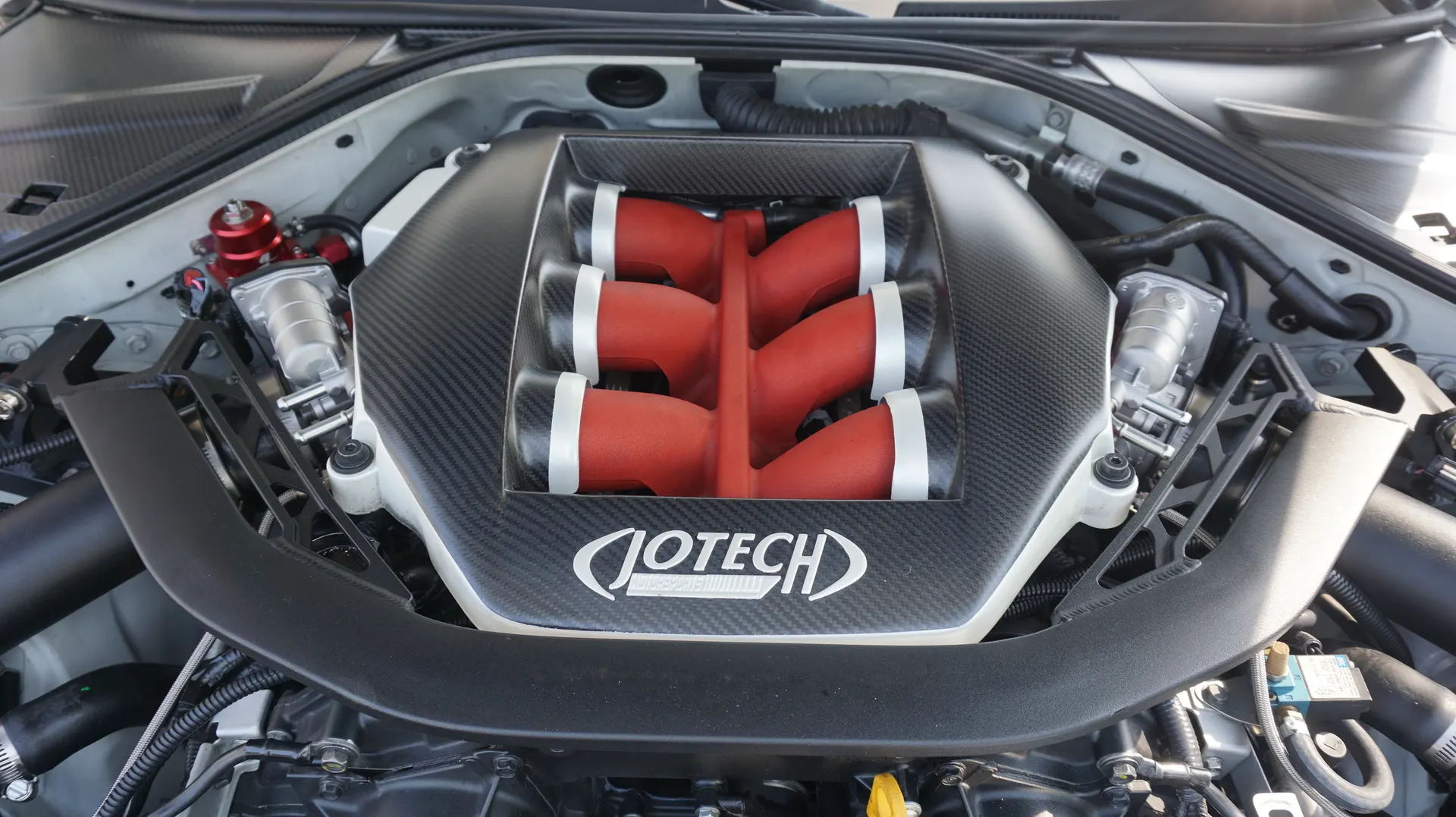 A close-up of a Jotech tuned Nissan GT-R engine bay featuring a carbon fiber intake manifold and red runners.
