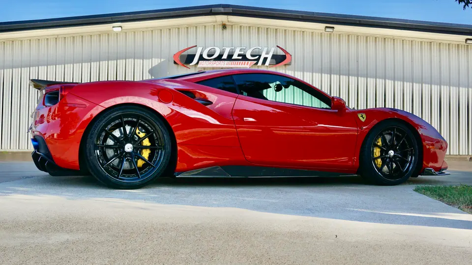 Red Ferrari 488 with aftermarket wheels, carbon fiber wing, and side skirts parked outside Jotech Motorsports.