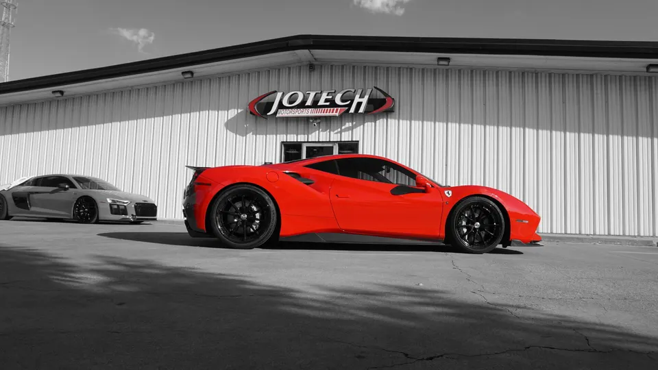 Red Ferrari 488 and grey Audi R8 parked outside Jotech Motorsports performance tuning shop.