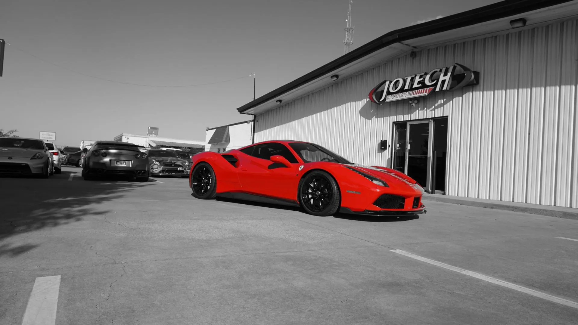 A red Ferrari 488 parked outside Jotech Motorsports performance tuning shop with other sports cars in the background.