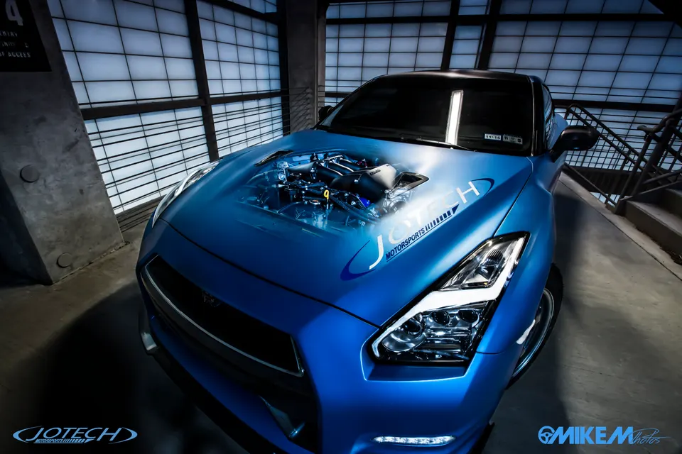 A blue Nissan GT-R with a custom hood graphic depicting its high-performance engine, parked in a modern, well-lit studio setting.