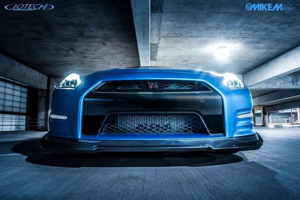 Front view of a blue Nissan GT-R with custom front splitter in a concrete parking garage.