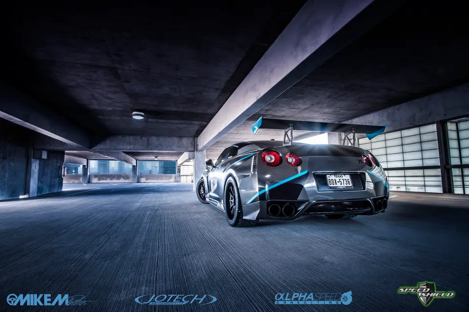 Modified Nissan GT-R with a large rear wing and blue accents parked in a concrete parking garage.