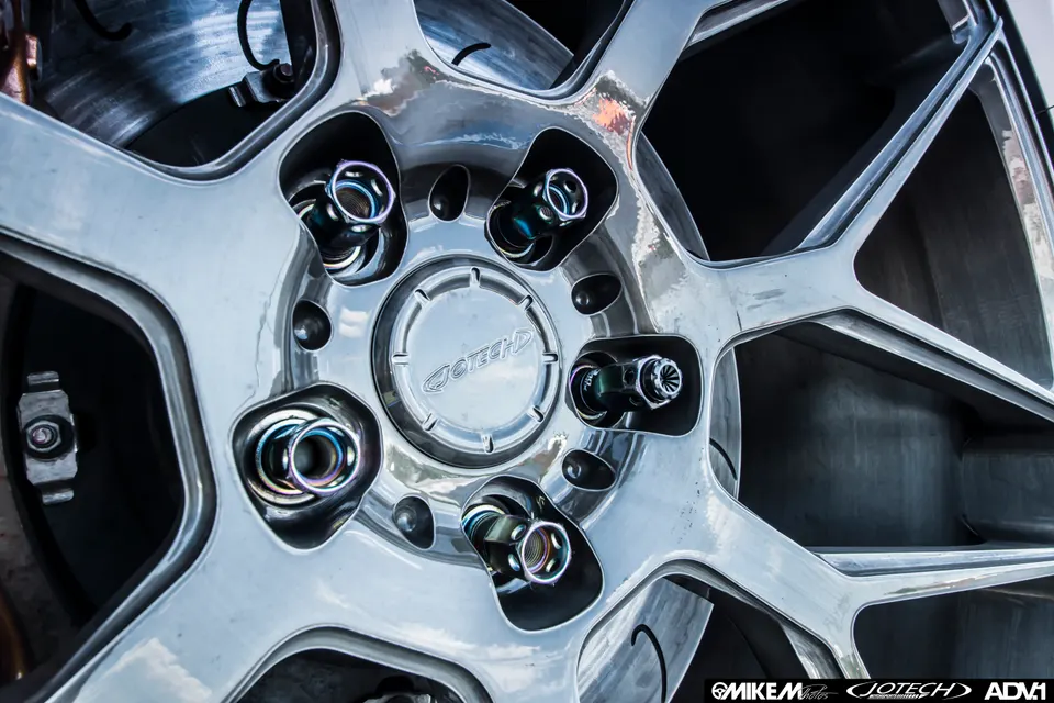 Close-up of a custom multi-spoke wheel with iridescent lug nuts and a Jotech center cap, showing brake rotor.