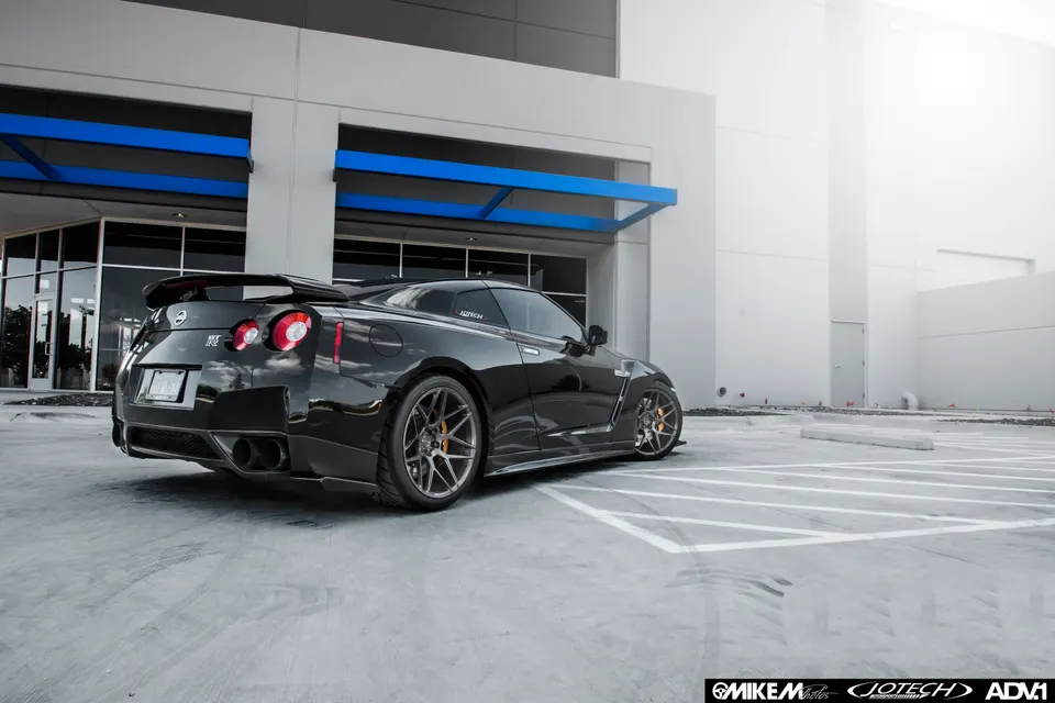 Black Nissan GT-R with custom wheels parked in a modern building's parking lot, showcasing its sleek design.