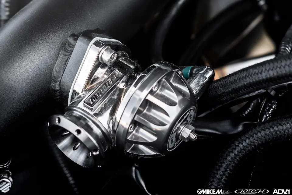 A close-up shot of a Tial blow-off valve installed in an engine bay, showcasing the polished finish and boost piping.