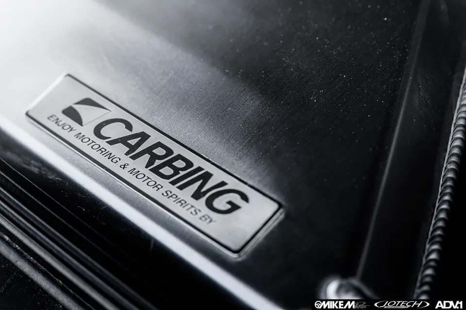 A close-up detail shot of a Carbing brand badge on a brushed metal performance car part.