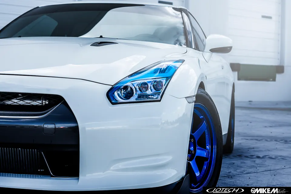 Front quarter view of a white Nissan GT-R with custom blue wheels and blue-tinted headlights in a clean setting.