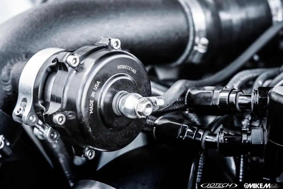 A close-up detail shot of a black blow-off valve with 'MADE IN USA' text in a performance car's engine bay.