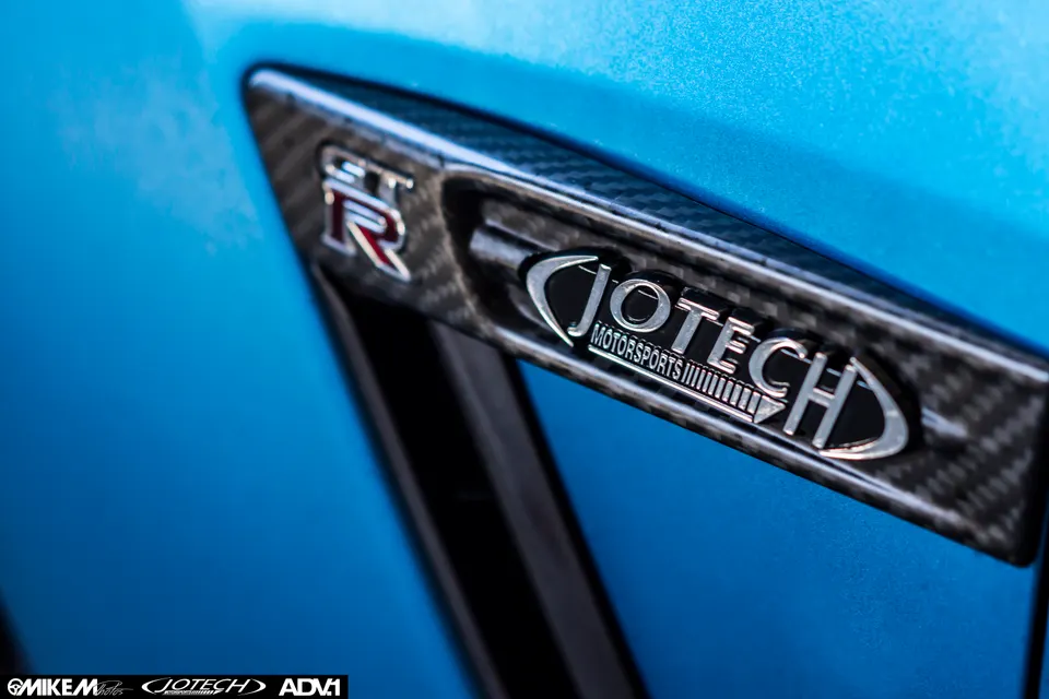 A close-up of a blue Nissan GT-R fender vent with carbon fiber trim and Jotech Motorsports badge.