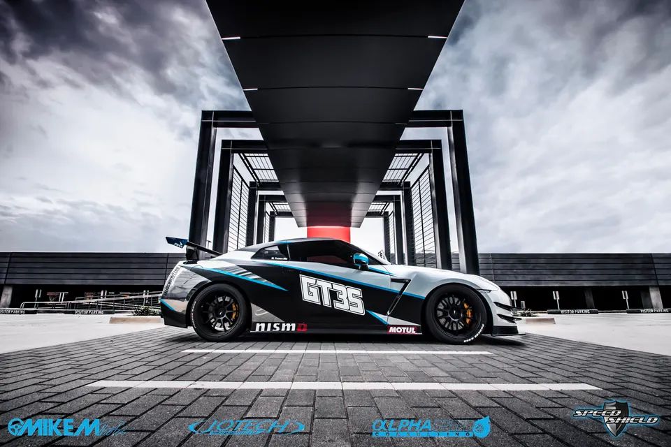 A highly modified Nissan GT-R with a black and blue custom livery and aftermarket wheels, parked in a modern architectural setting.