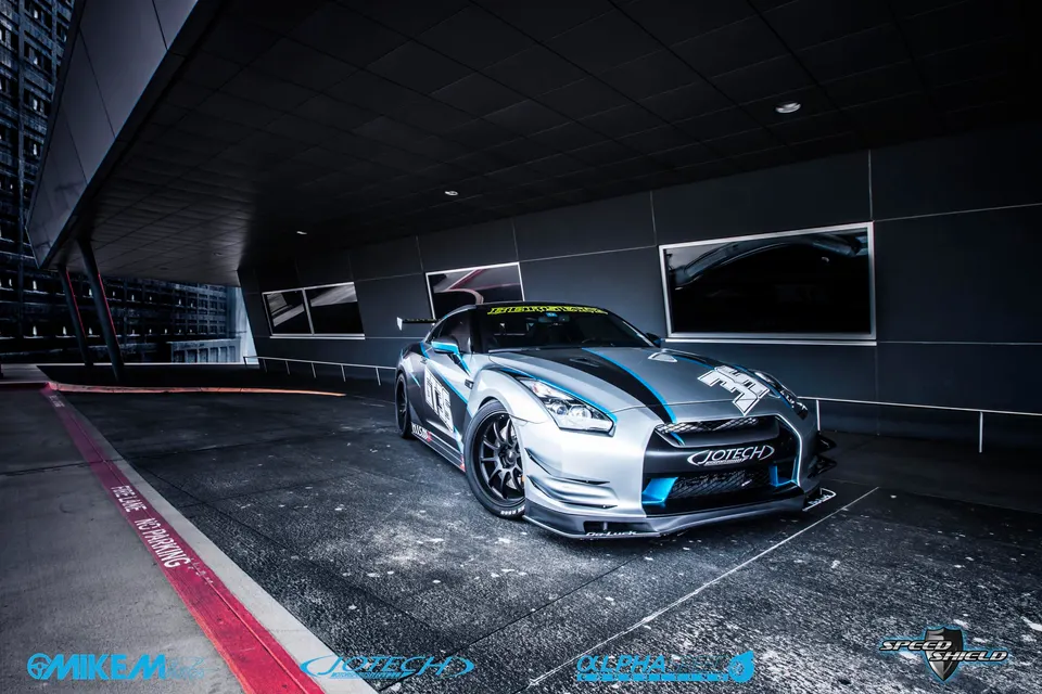 Silver Nissan GT-R with blue accents and an aero kit parked in a modern architectural setting.