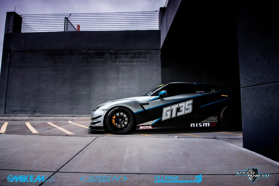 A Nissan GT-R with a silver and black custom wrap and GT35 livery parked in an urban setting.