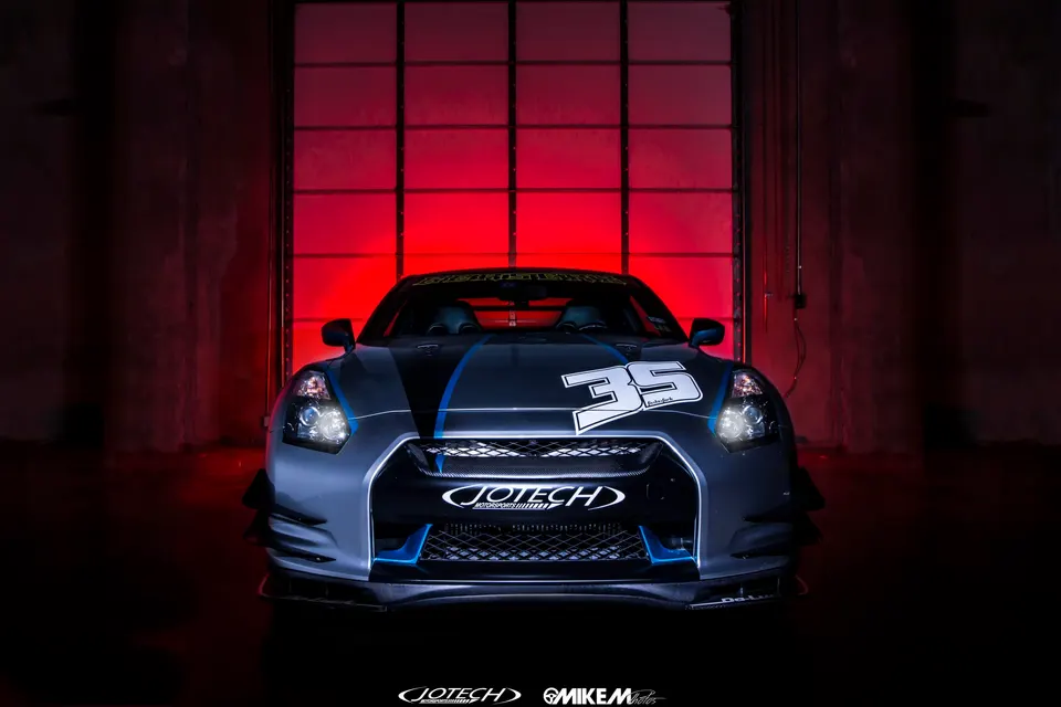 A front view of a custom gray and blue Nissan GT-R with Jotech branding and number 35 on the hood, professionally lit with a red background.