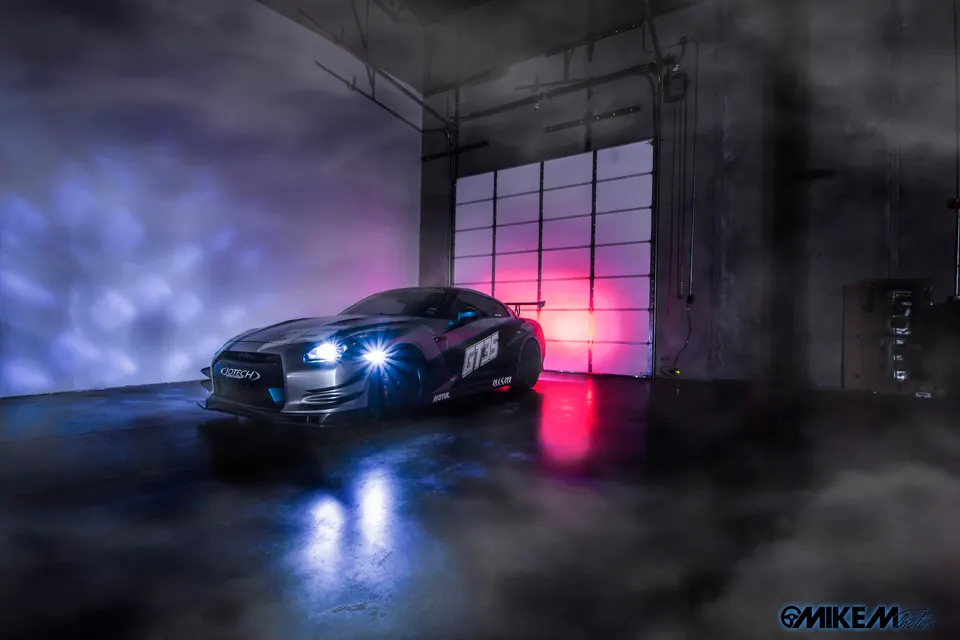 A wide shot of a modified Nissan GT-R R35 with a widebody kit and custom lighting in a studio setting.