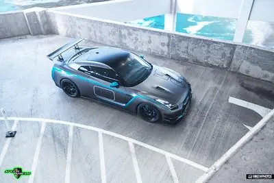 A grey Nissan GT-R with blue accents and a large rear wing parked in a concrete parking structure.