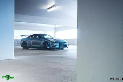A modified gray Nissan GT-R R35 with custom wheels and aero parked in a brightly lit parking garage.