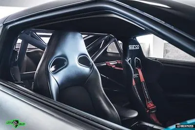 Interior view of a performance car featuring Sparco racing seats, red harnesses, and a custom roll cage.
