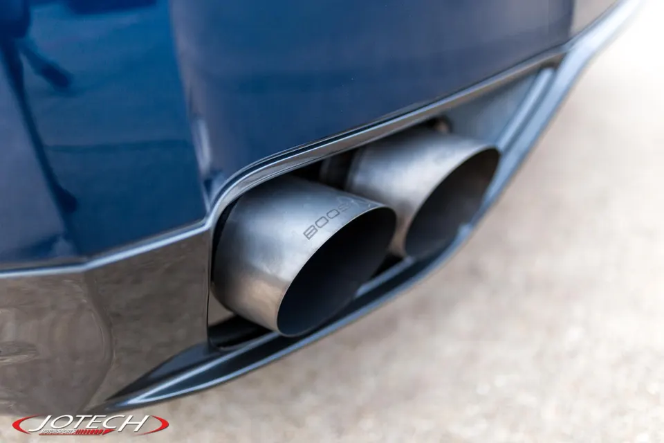 Close-up of custom "BOOST" exhaust tips on a blue performance car, highlighting the rear bumper detail.