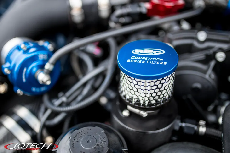Close-up of a performance engine bay showing a blue RBC Competition Series air filter and a blow-off valve.