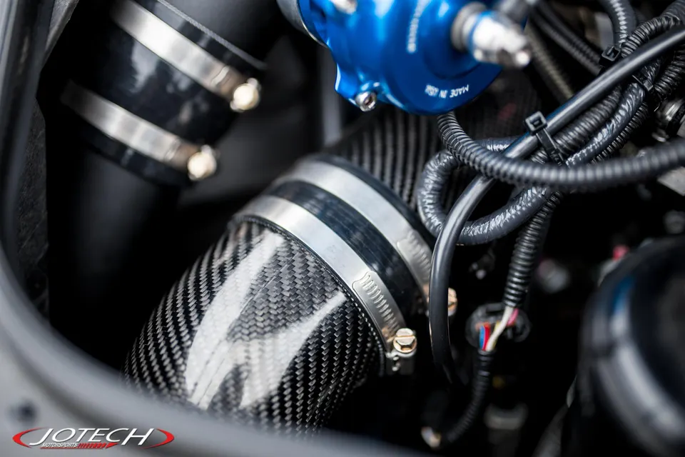 Close-up of a carbon fiber intake pipe and a blue blow-off valve in a high-performance engine bay.