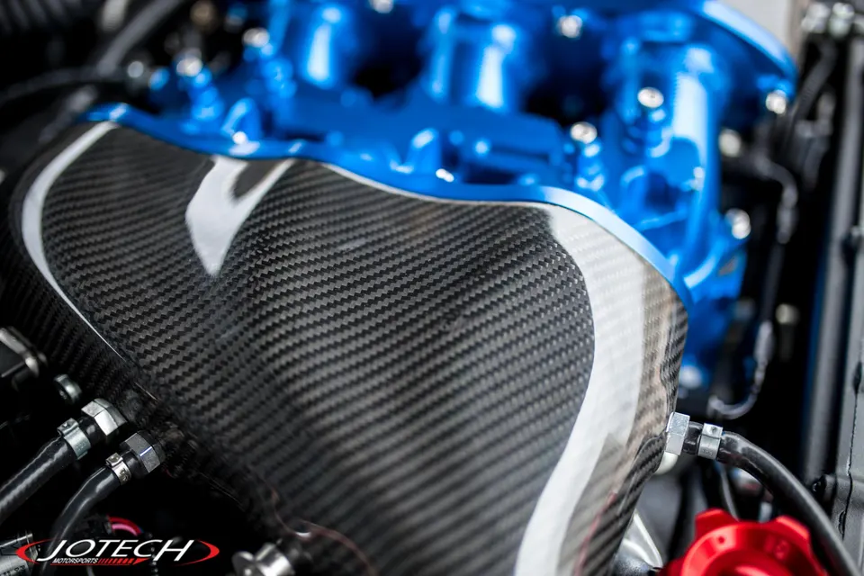 Close-up of a custom engine bay featuring a carbon fiber intake manifold and a blue painted intake manifold.