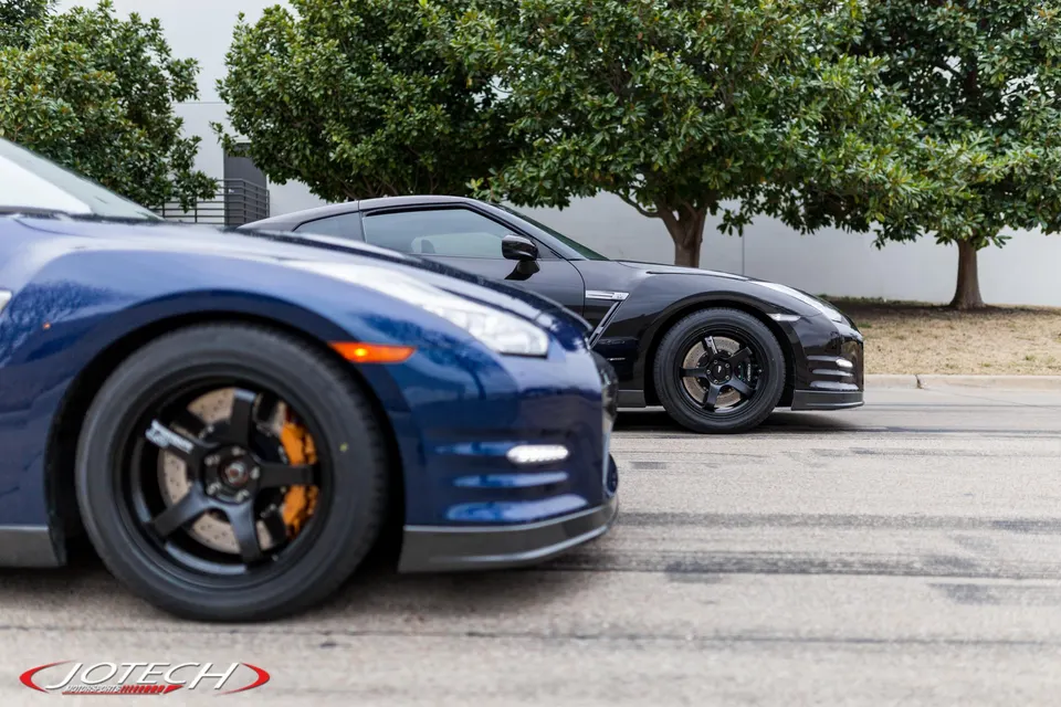 Two Nissan GT-Rs, one blue and one black, parked outdoors showcasing aftermarket wheels and performance brakes.