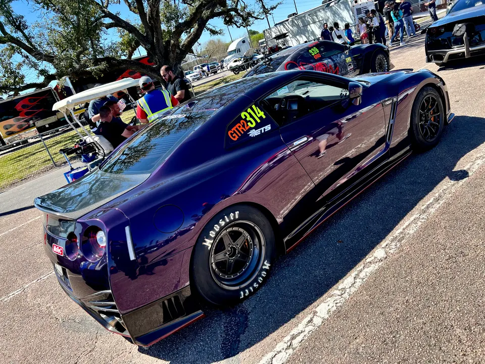 Purple Nissan GT-R with Hoosier drag tires and carbon fiber aero at a drag strip staging lane.