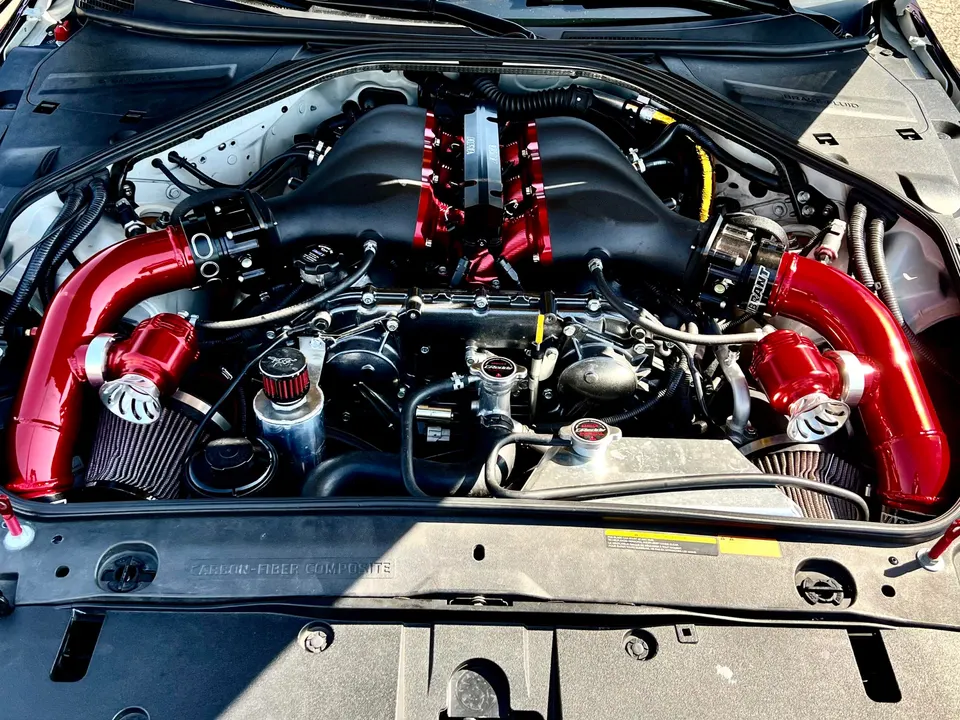 Close-up of a modified Nissan GT-R engine bay featuring red aftermarket boost pipes, air filters, and blow-off valves.
