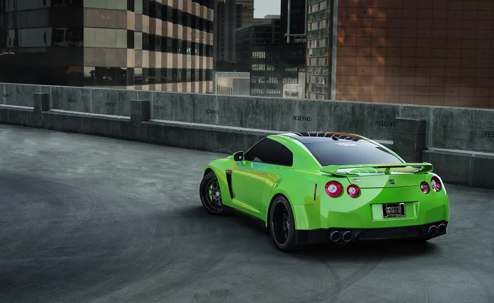 A bright green Nissan GT-R R35 with aftermarket wheels and exhaust parked on a rooftop with city buildings in the background.