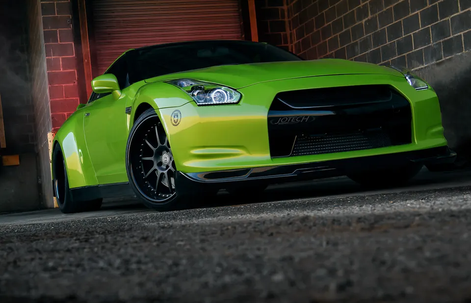 Bright green Nissan GT-R with aftermarket HRE wheels and Jotech branding, featuring a front splitter, in a professional photoshoot setting.