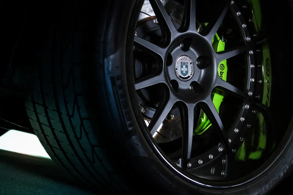 A close-up of a black HRE performance wheel with a vibrant green Brembo brake caliper and a performance tire.
