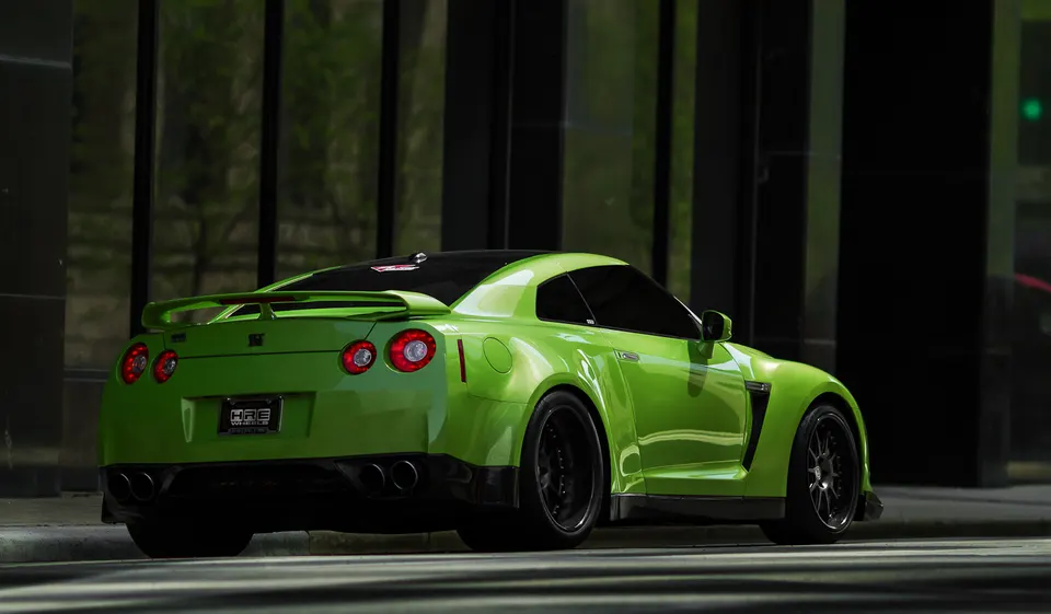 A vibrant green Nissan GT-R with HRE wheels and a custom exhaust system parked on a city street.