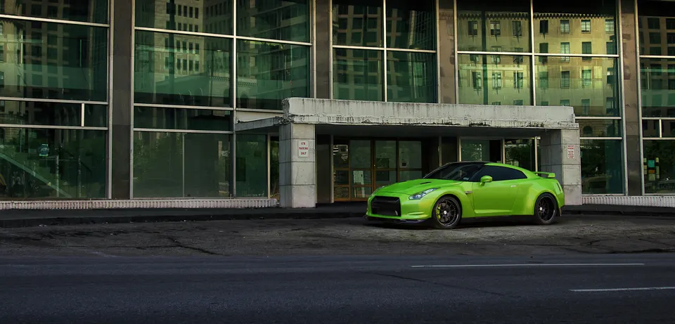 A vibrant green Nissan GT-R is parked on a paved area in front of a modern building with large glass windows.