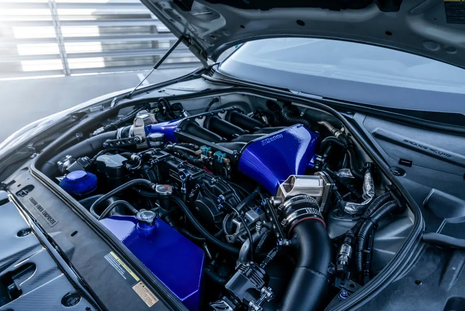 Close-up view of a modified Nissan GT-R engine bay featuring a blue aftermarket induction system and performance parts.