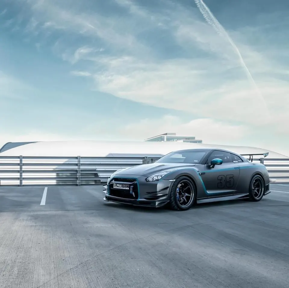 A grey Nissan GT-R with blue accents and an aftermarket aero kit parked on a rooftop.