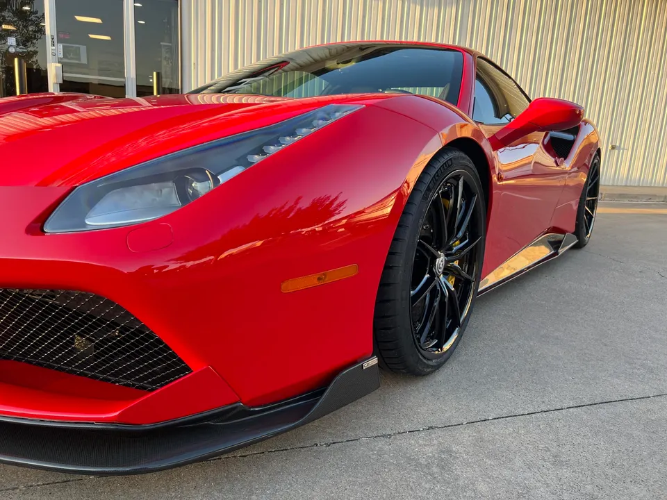 A gleaming red Ferrari 488 with carbon fiber aero enhancements and black wheels parked outside a building.