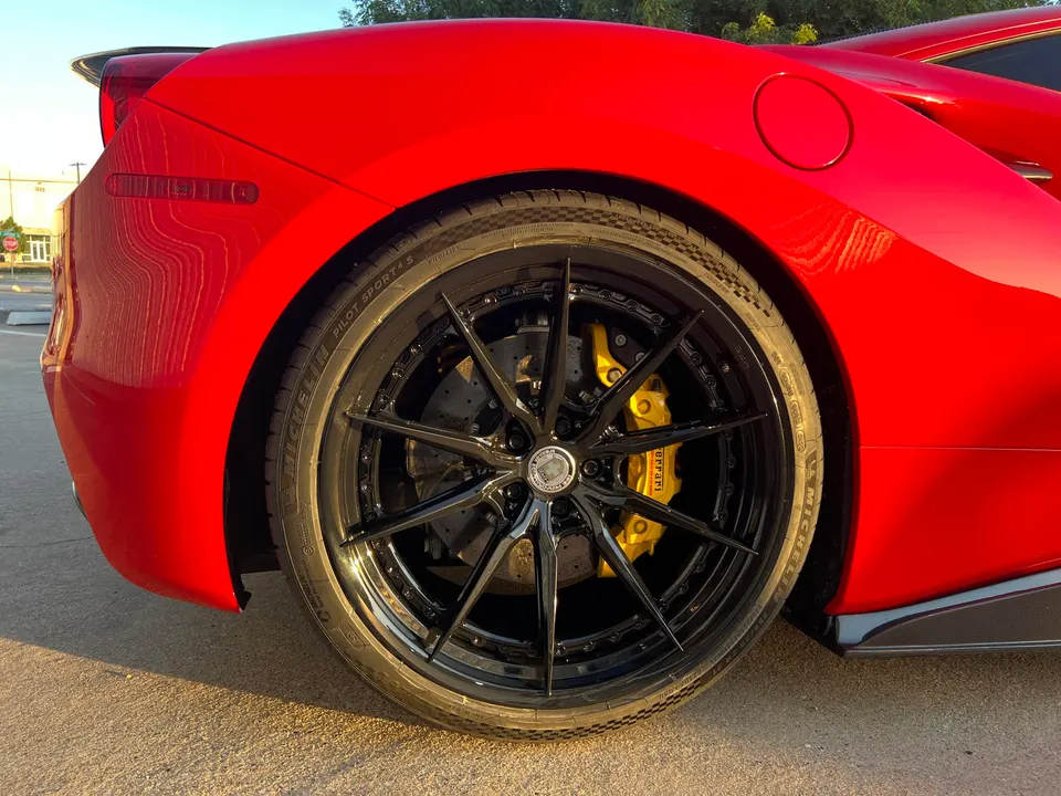 Close-up of a red Ferrari's rear wheel with black multi-spoke wheels, yellow brake calipers, and Michelin Pilot Sport 4S tires.