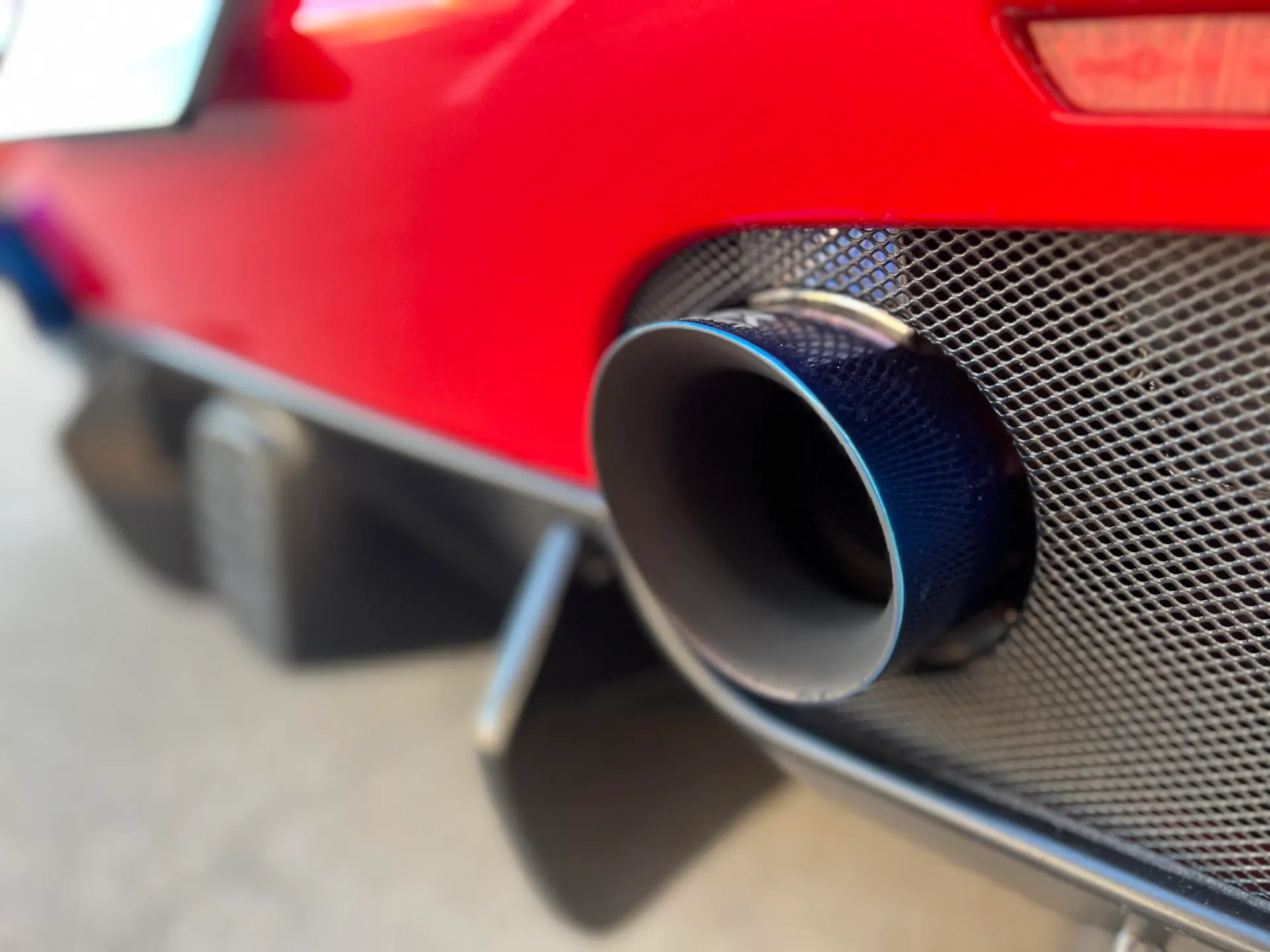 Close-up of a blue titanium exhaust tip and carbon fiber diffuser on a red sports car.