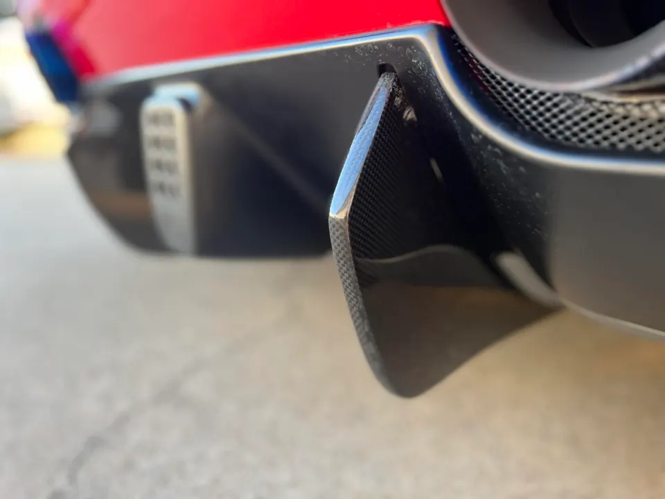 Close-up of a red supercar's carbon fiber rear diffuser and exhaust tip.