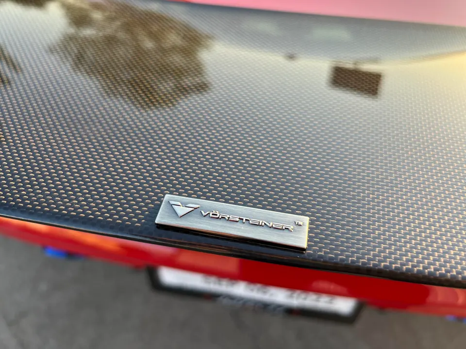Close-up of a Vorsteiner carbon fiber rear spoiler on a red performance car.