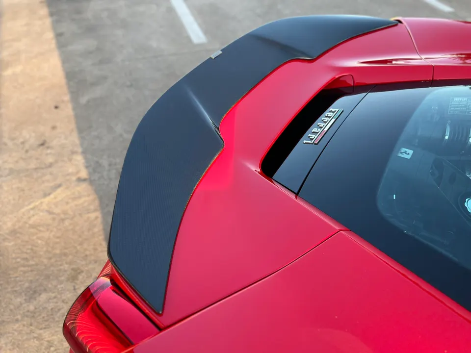Close-up of a red Ferrari's carbon fiber rear spoiler and engine bay, showcasing aerodynamic details.
