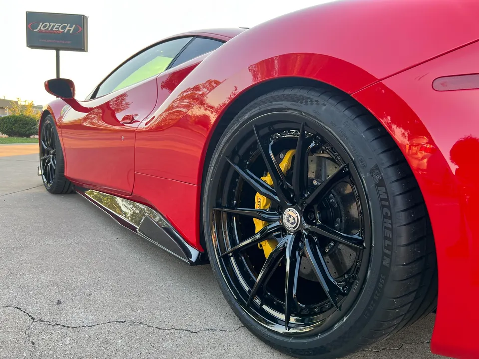A red Ferrari with black HRE wheels, yellow brake calipers, and carbon side skirts parked outside Jotech Motorsports.