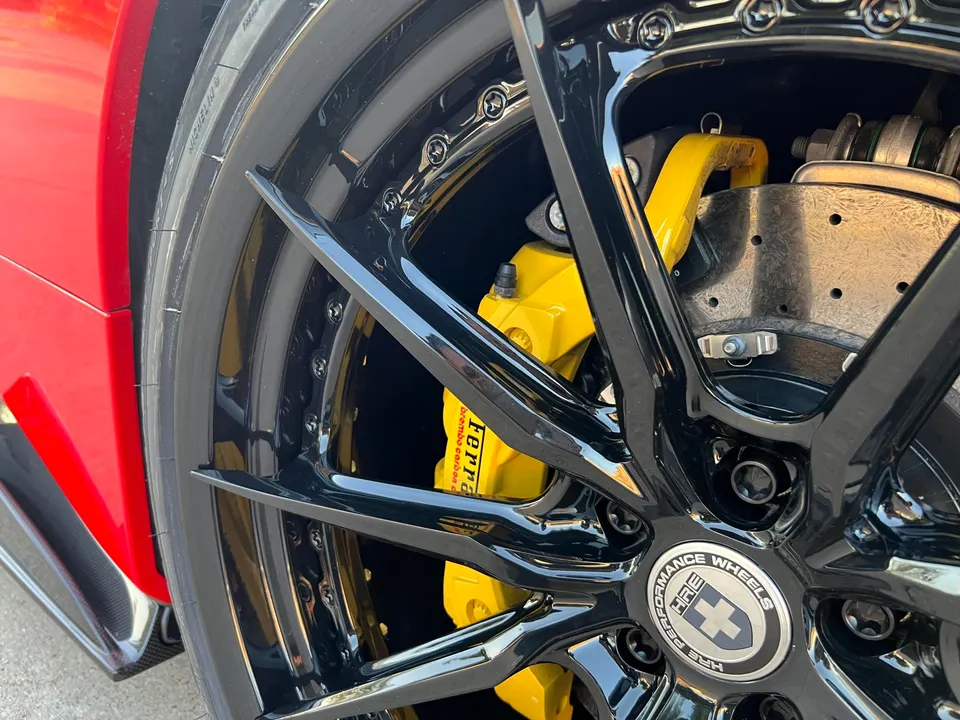 Close-up of a red car's black HRE Performance Wheels, yellow Ferrari Brembo brake calipers, and Michelin tires.