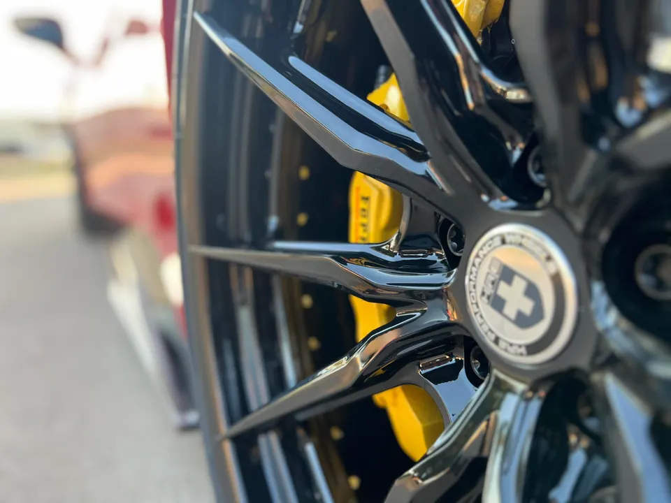 Close-up of a black HRE performance wheel with yellow Ferrari brake calipers on a luxury sports car.