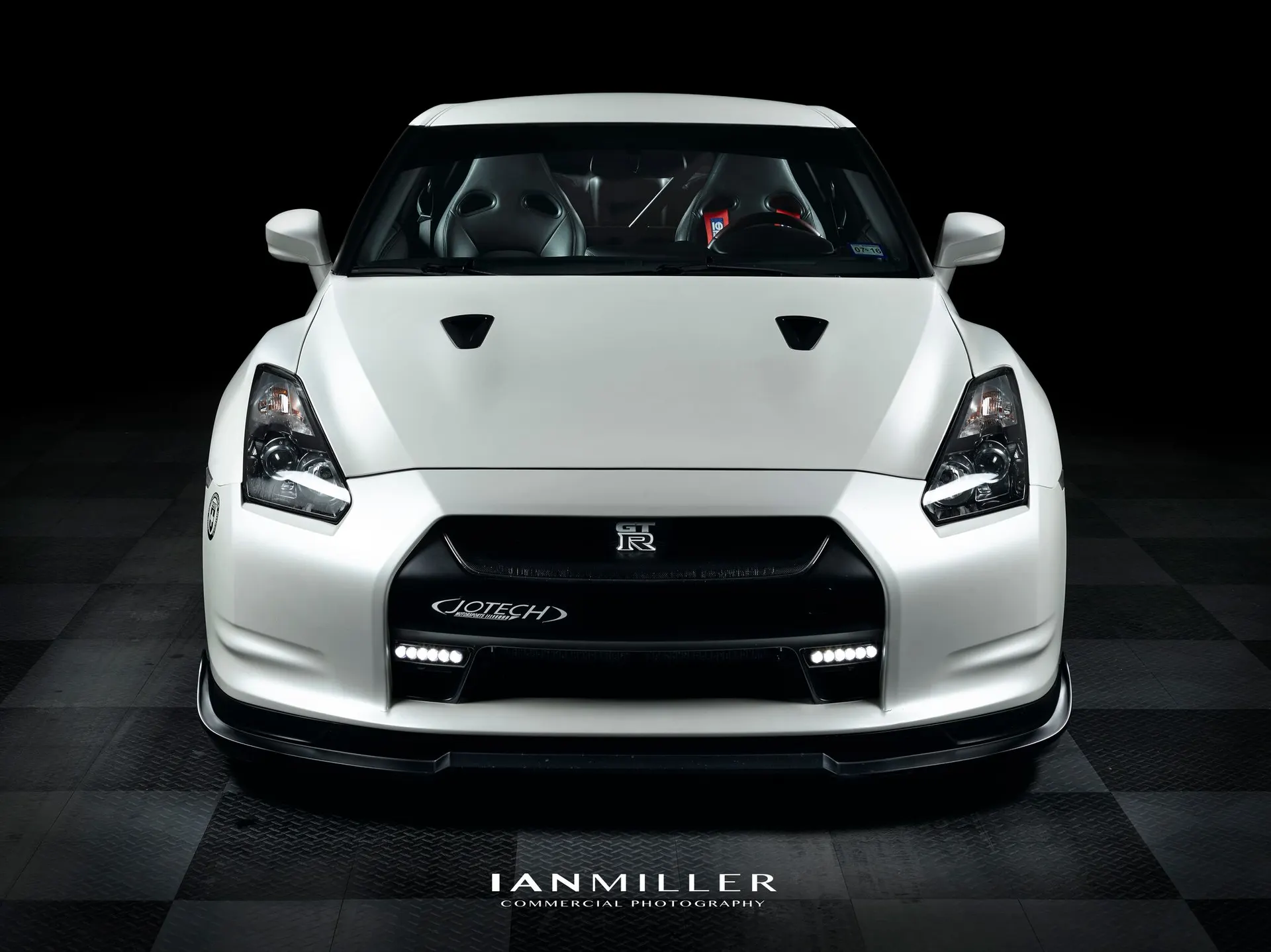 A white Nissan GT-R with Jotech branding on the front bumper, professionally photographed in a studio setting.